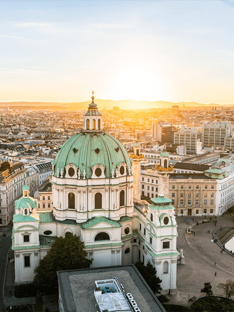 Historic cityscape view of St. Charles Church with distinctive green dome in Vienna at sunset.
