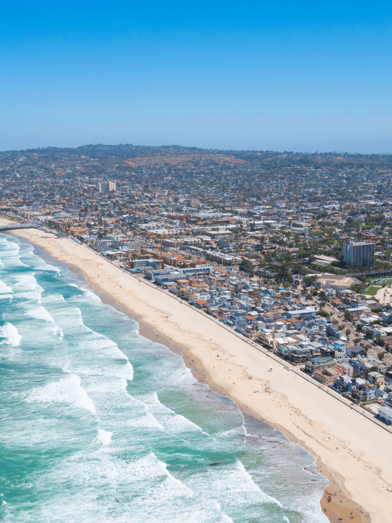 Aerial view of a sunny Los Angeles beach with waves and beachfront homes on the coast.