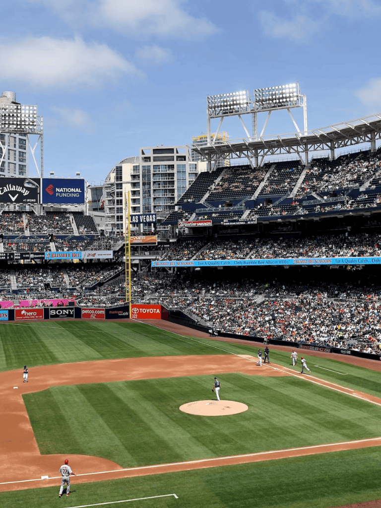 Outdoor baseball stadium with active game, covered seating, and vibrant city backdrop.