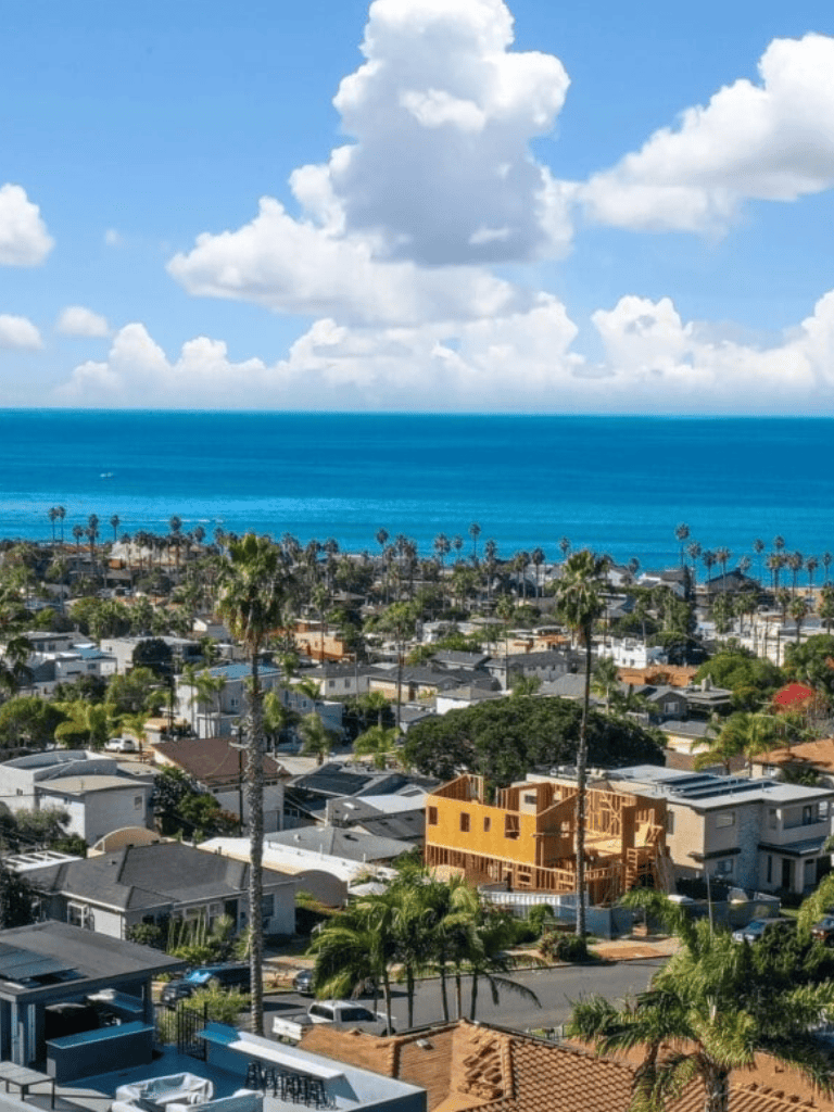 Vibrant coastal neighborhood with newly built homes near the ocean and palm trees under blue sky.