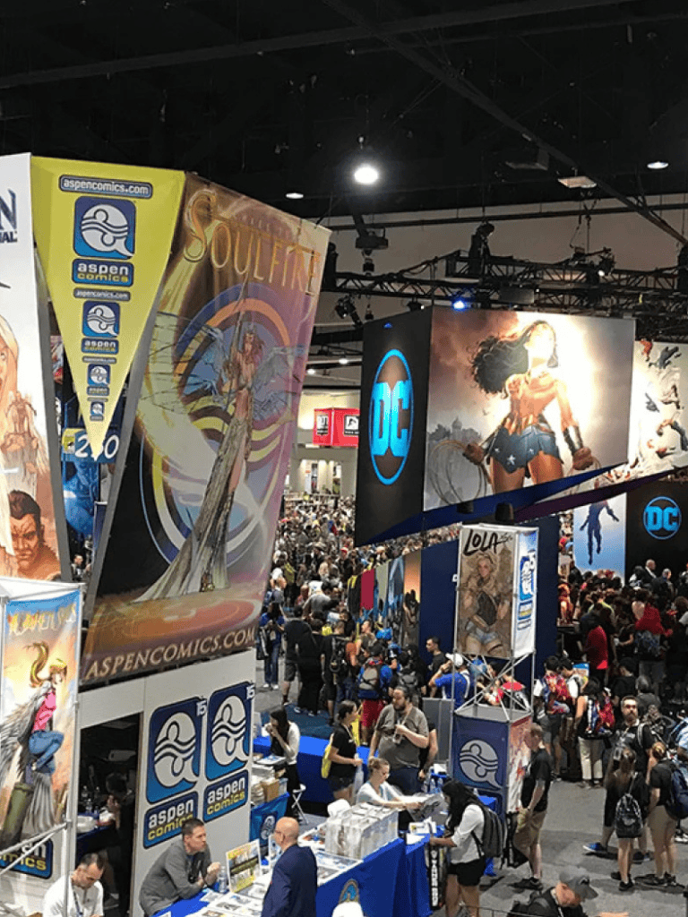 Avertized comic convention booth showcasing popular DC comics characters and colorful artwork, crowded event space for comic fans.