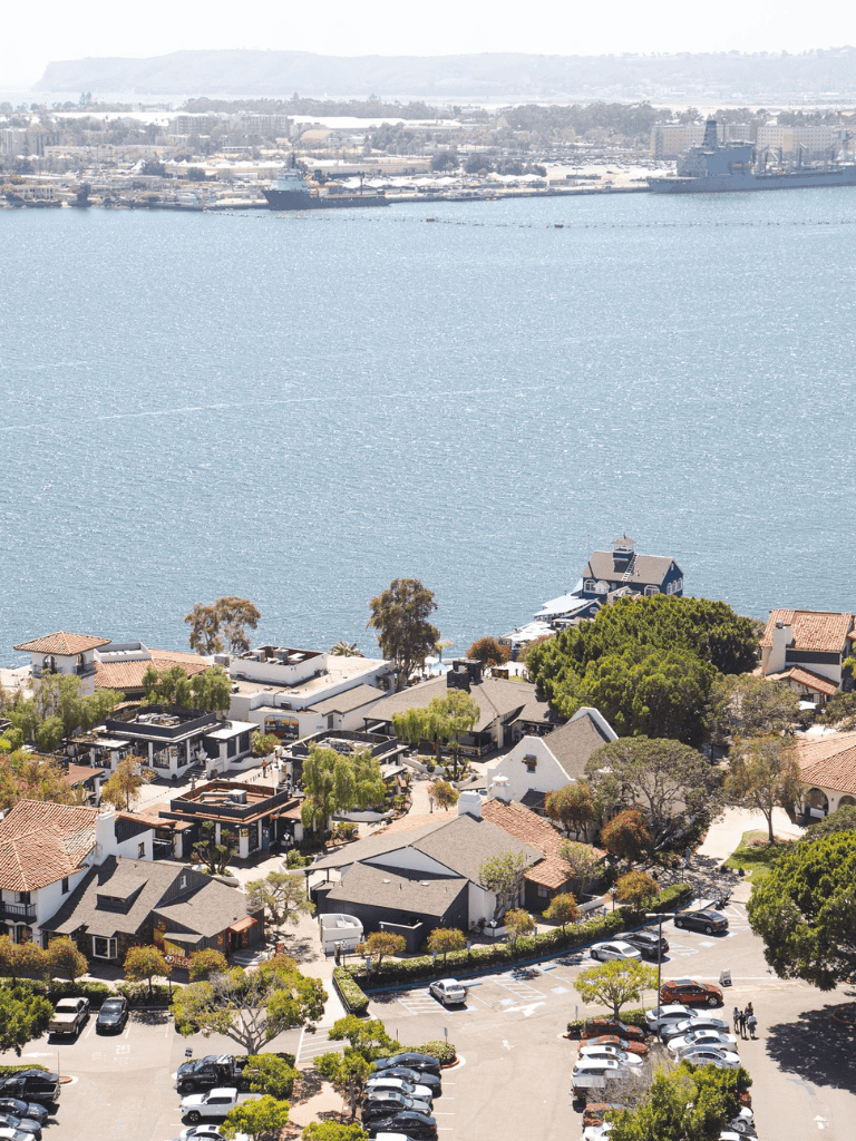 Boat and harbor view of coastal neighborhood with residential homes and parking lot, seawater, and shipping vessels.