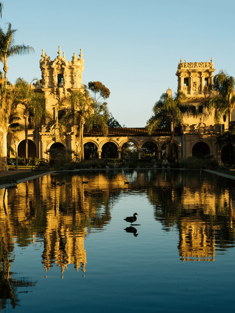 Elegant historic building reflecting in a scenic pond with ducks, surrounded by palm trees at QuestForDirections.