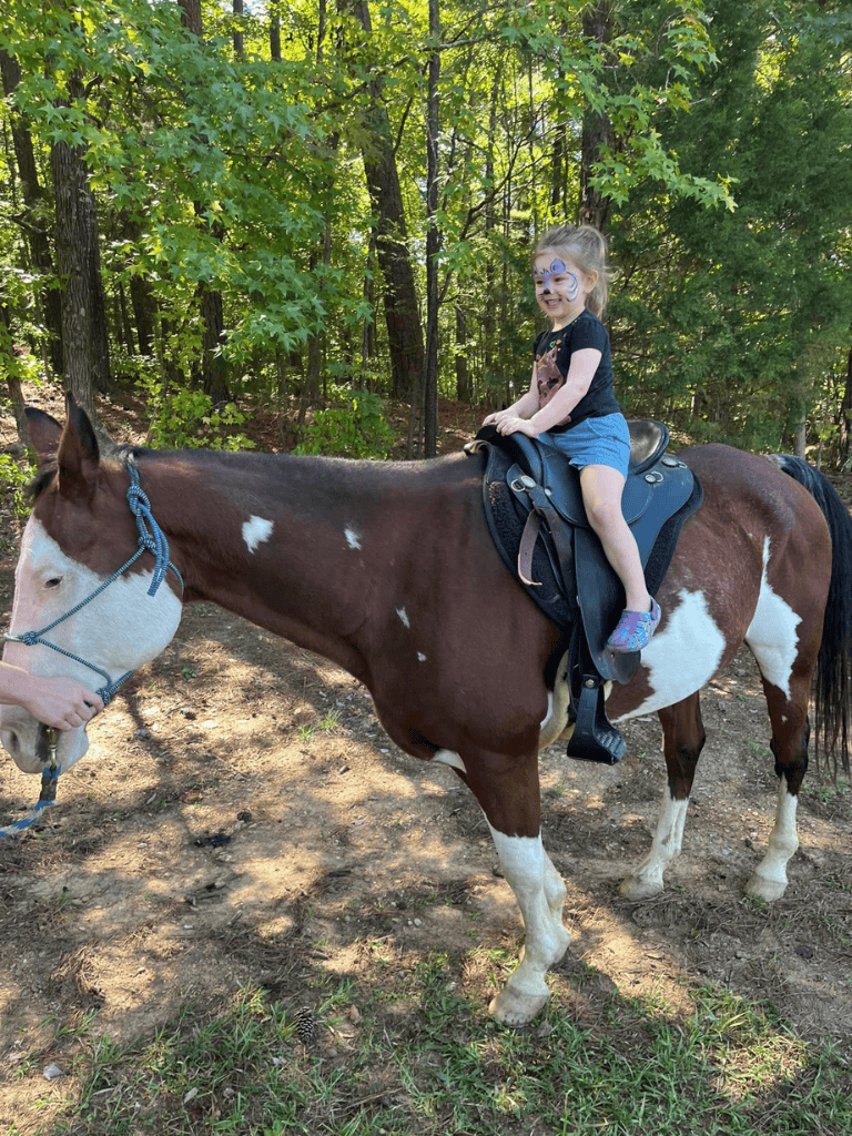 Child riding a horse on a trail surrounded by trees, outdoor adventure, family fun, equestrian activities.