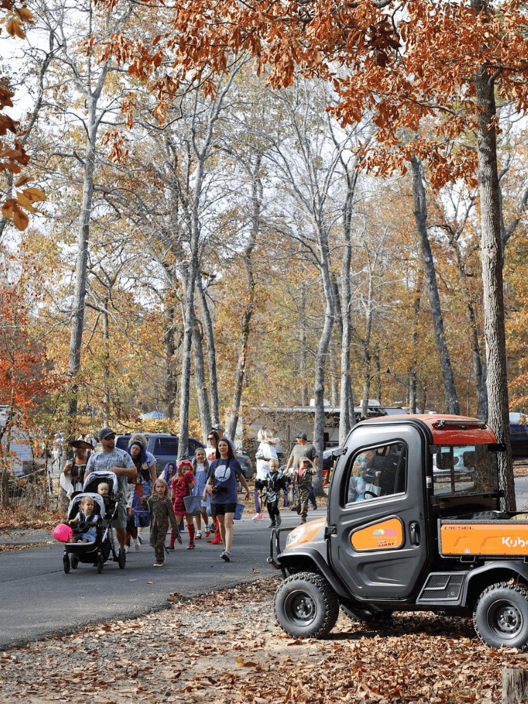 Enthusiastic crowd exploring outdoors in scenic fall forest, guided by electric utility vehicle.