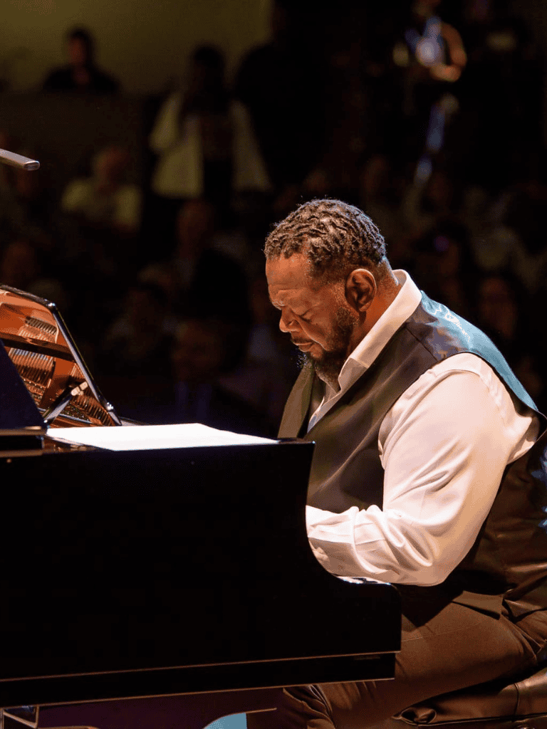 Playing grand piano at a live music event with audience in the background.