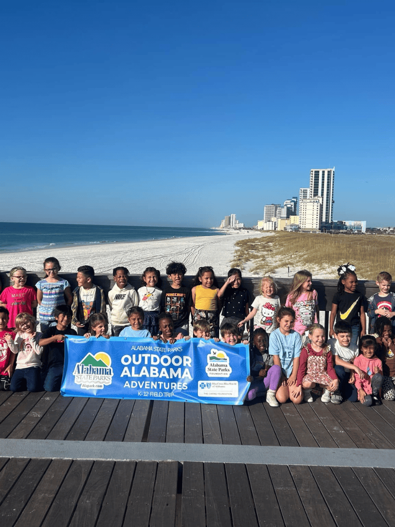 Kids at Alabama outdoor adventure camp by the beach, enjoying a group photo on the boardwalk.