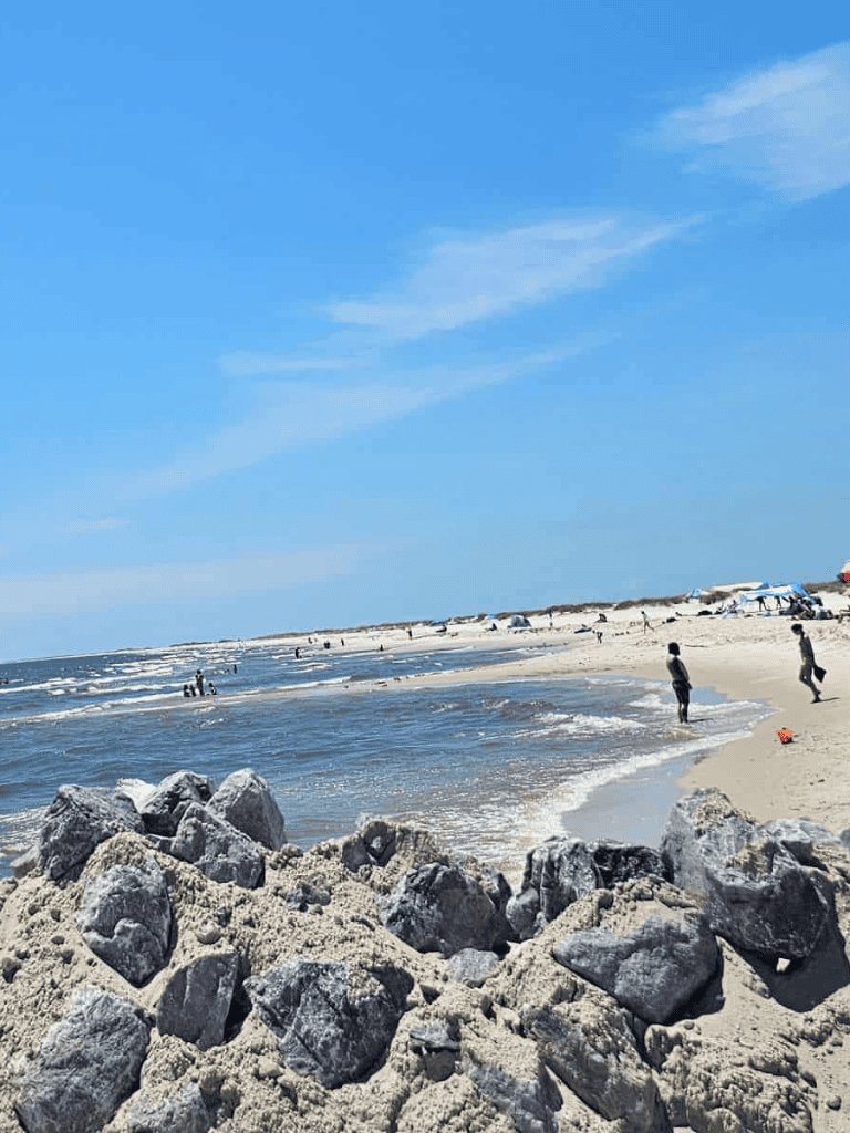 Bright sunny beach with rocks, sand, and people enjoying the ocean, ideal for seaside adventures and relaxation.