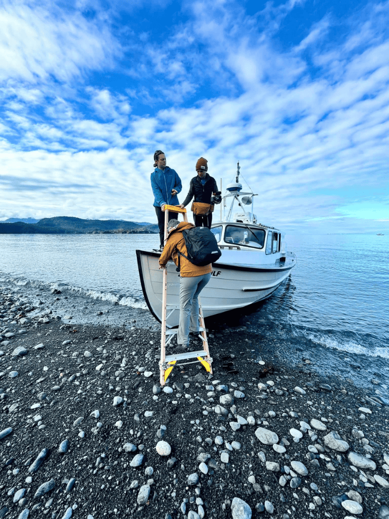 Boat passenger boarding along rocky shoreline with scenic sky, promoting travel guidance by QuestForDirections.