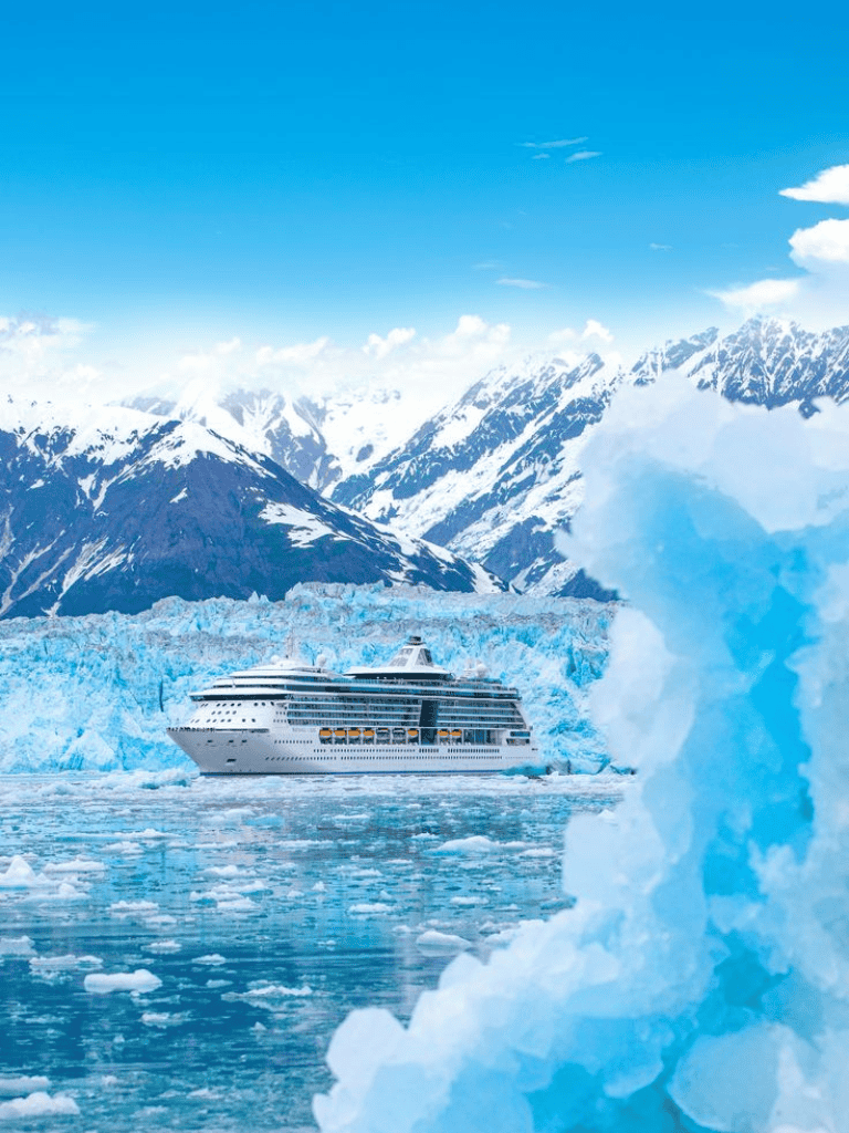 Iceberg and cruise ship in icy Arctic waters with snow-covered mountains in the background.