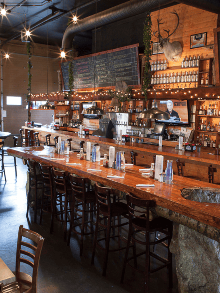 Cozy rustic restaurant featuring a long wooden bar, mounted deer head, and warm ambient lighting for a welcoming dining experience.