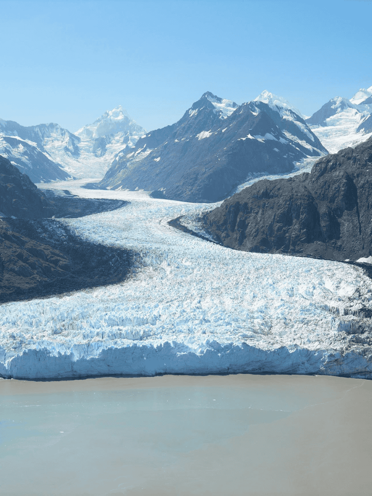 Stunning glacier melting into turquoise lake amidst rugged mountain landscape.