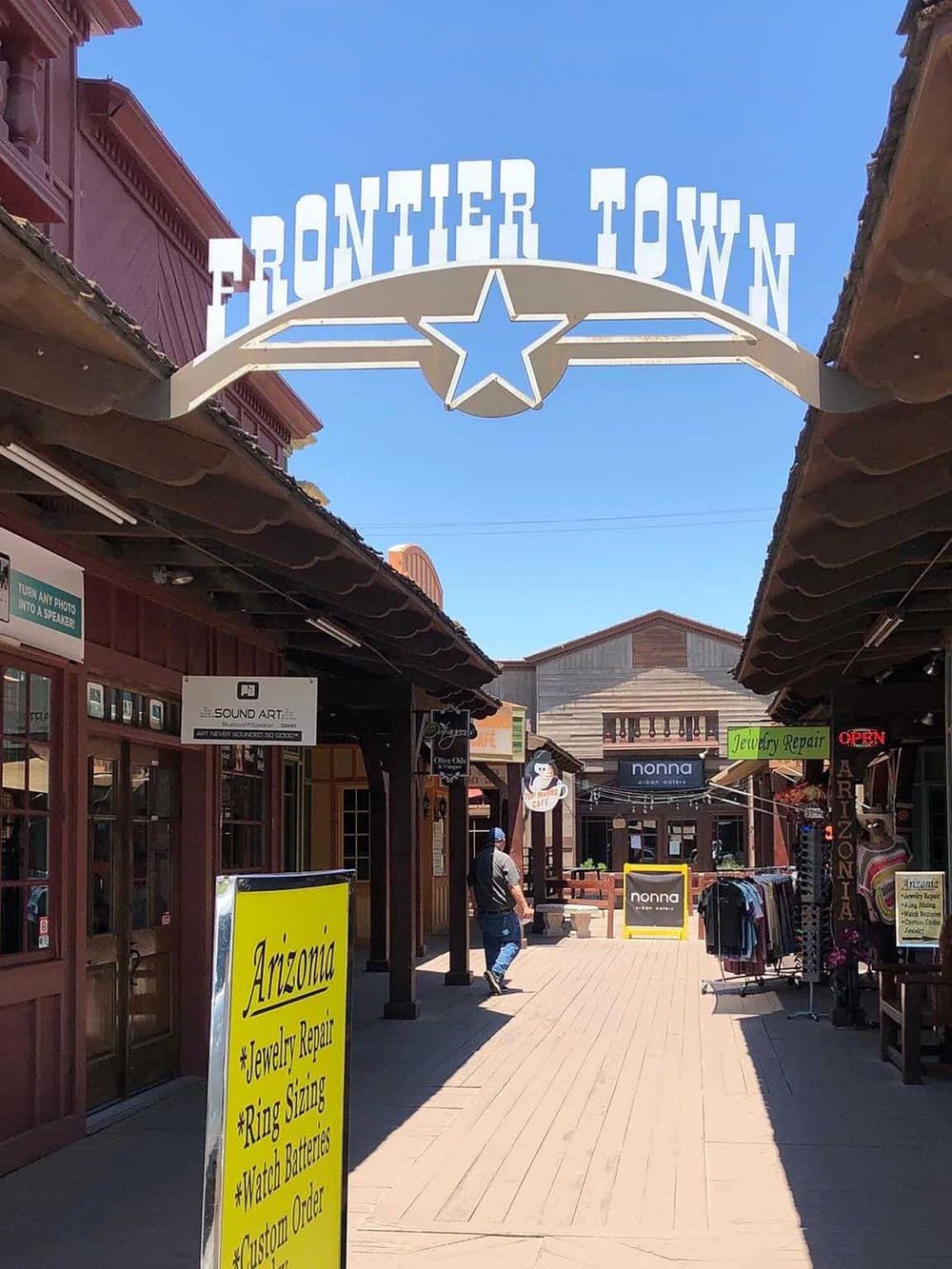 Colorful retail street in Frontier Town with shops, signs, and visitors, highlighting shopping and destination experiences.