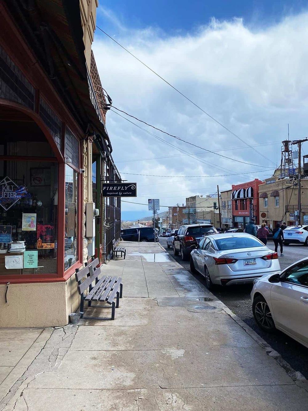 Busy downtown street with parked cars, storefronts, and cloudy sky, showcasing local navigation and directions.