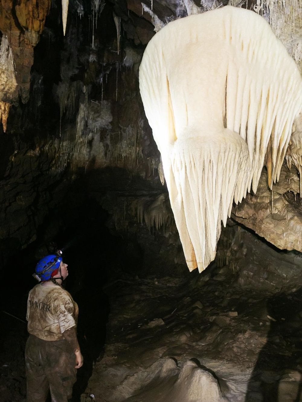 Stalactites inside a cave with a caver exploring the underground formation.