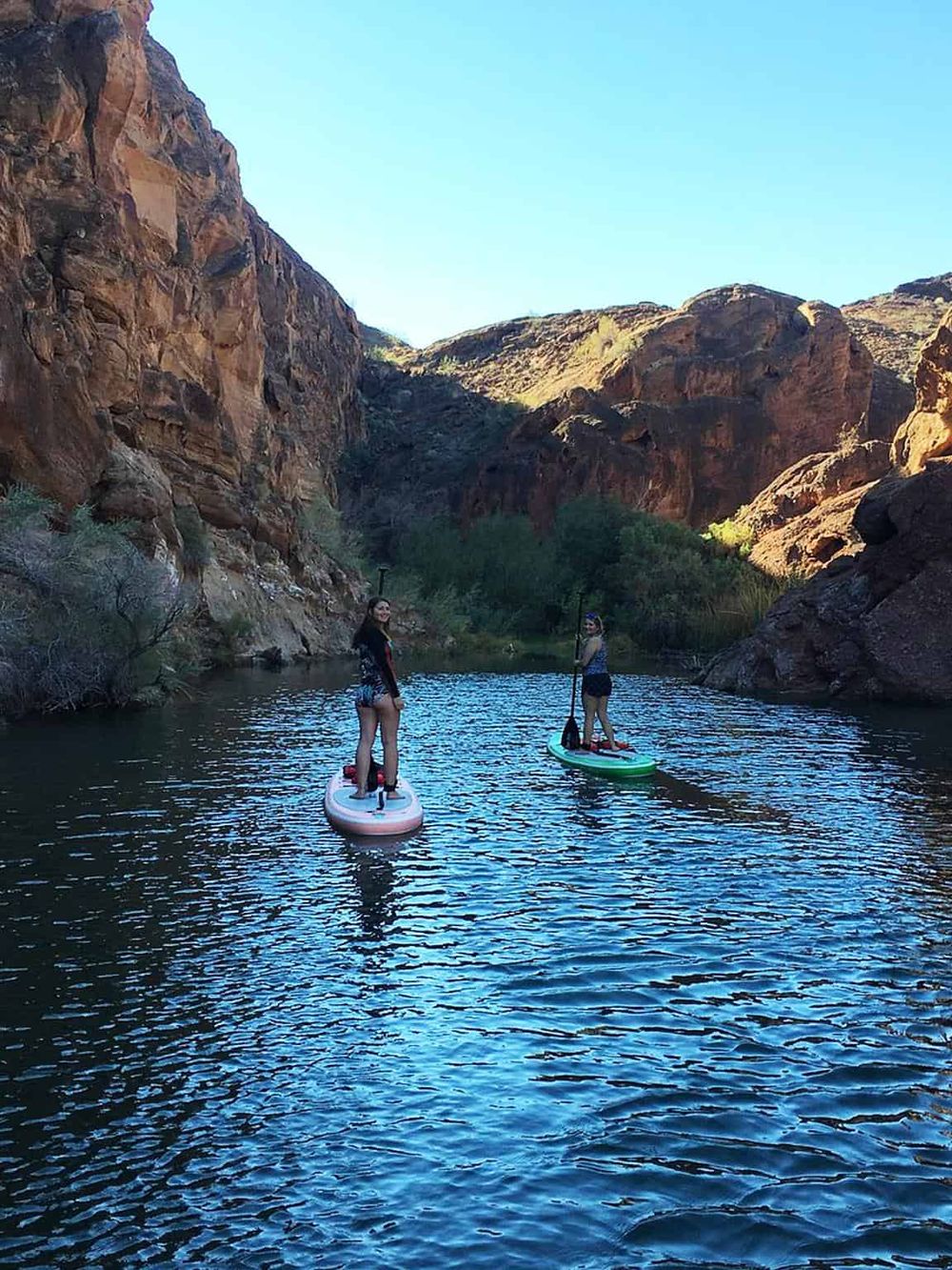 1. Women paddleboarding in a canyon river surrounded by rocky cliffs and desert landscape.