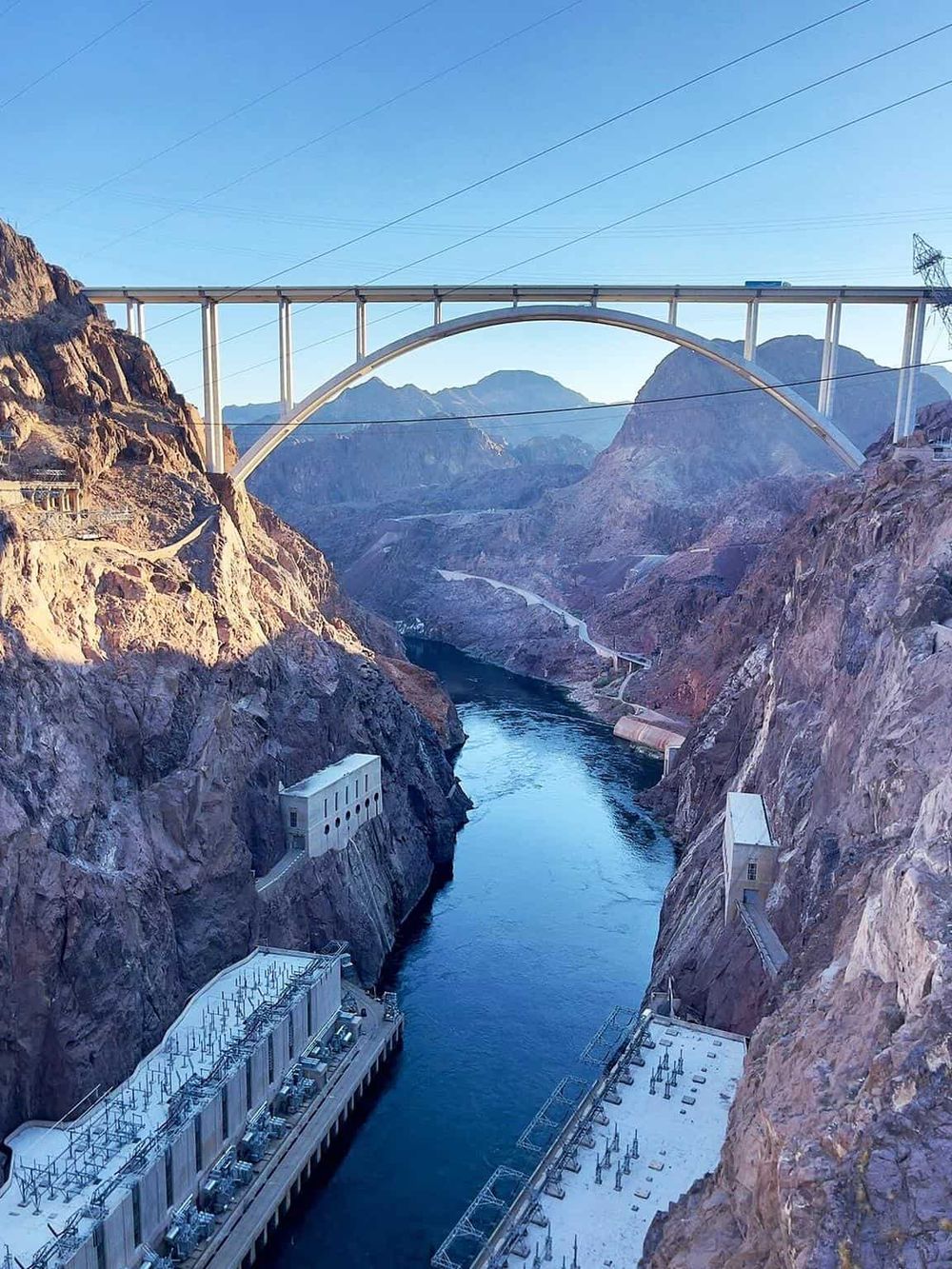 Impressive dam and bridge over a canyon with mountains in the background, showcasing engineering marvels and scenic views.