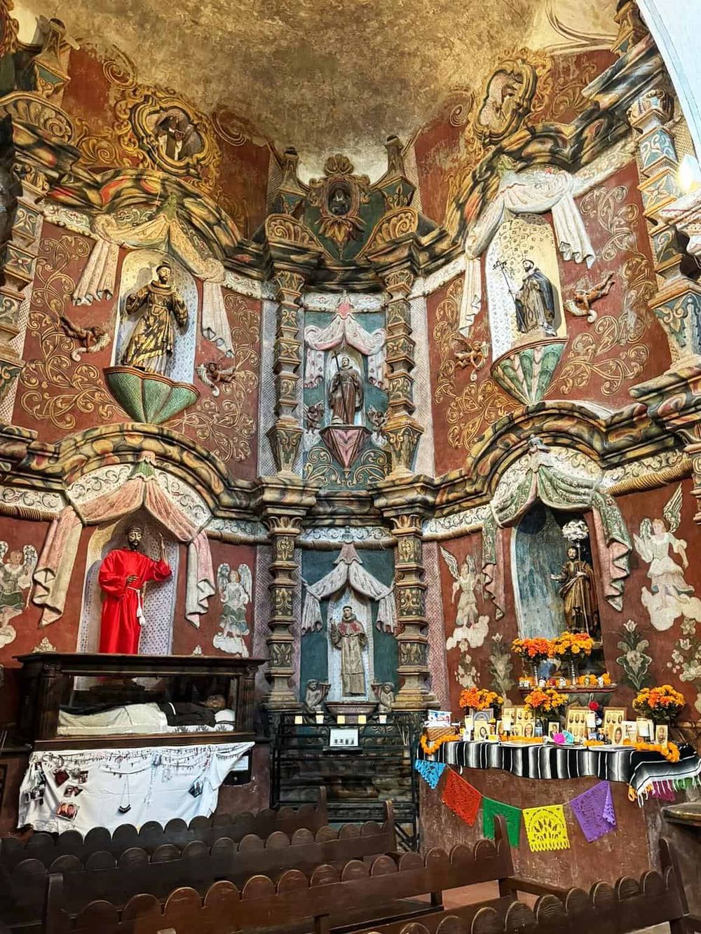 Colorful religious altar with vibrant murals and offerings in a church setting.