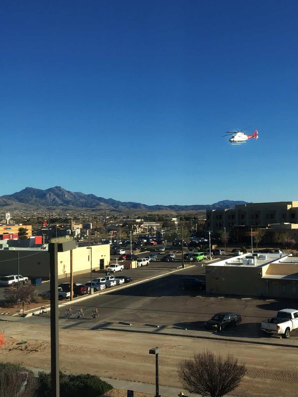 Helicopter flying over a city with mountain landscape in the background, daytime outdoor scene.