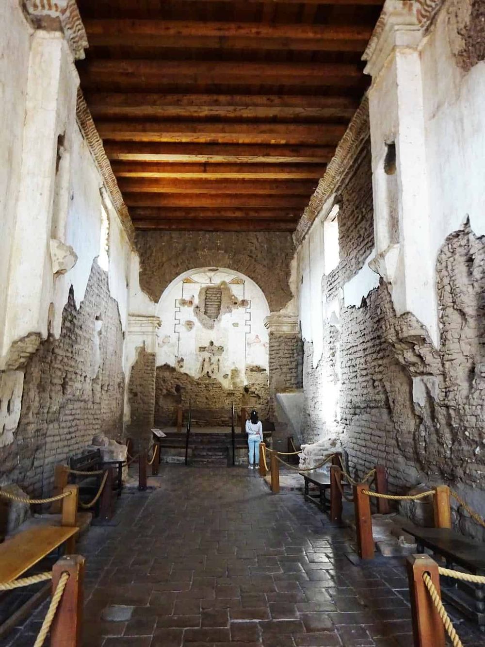 Ancient ruin interior with weathered brick walls, wooden ceiling, and archaeological exhibits.