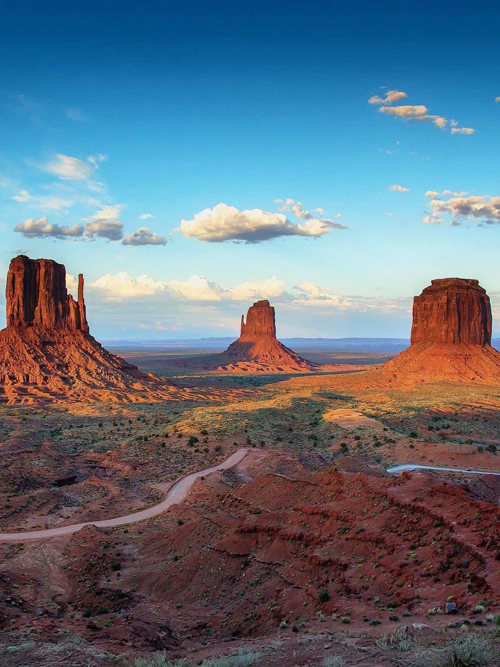 Three iconic buttes in Monument Valley under a bright blue sky, showcasing stunning desert landscape.