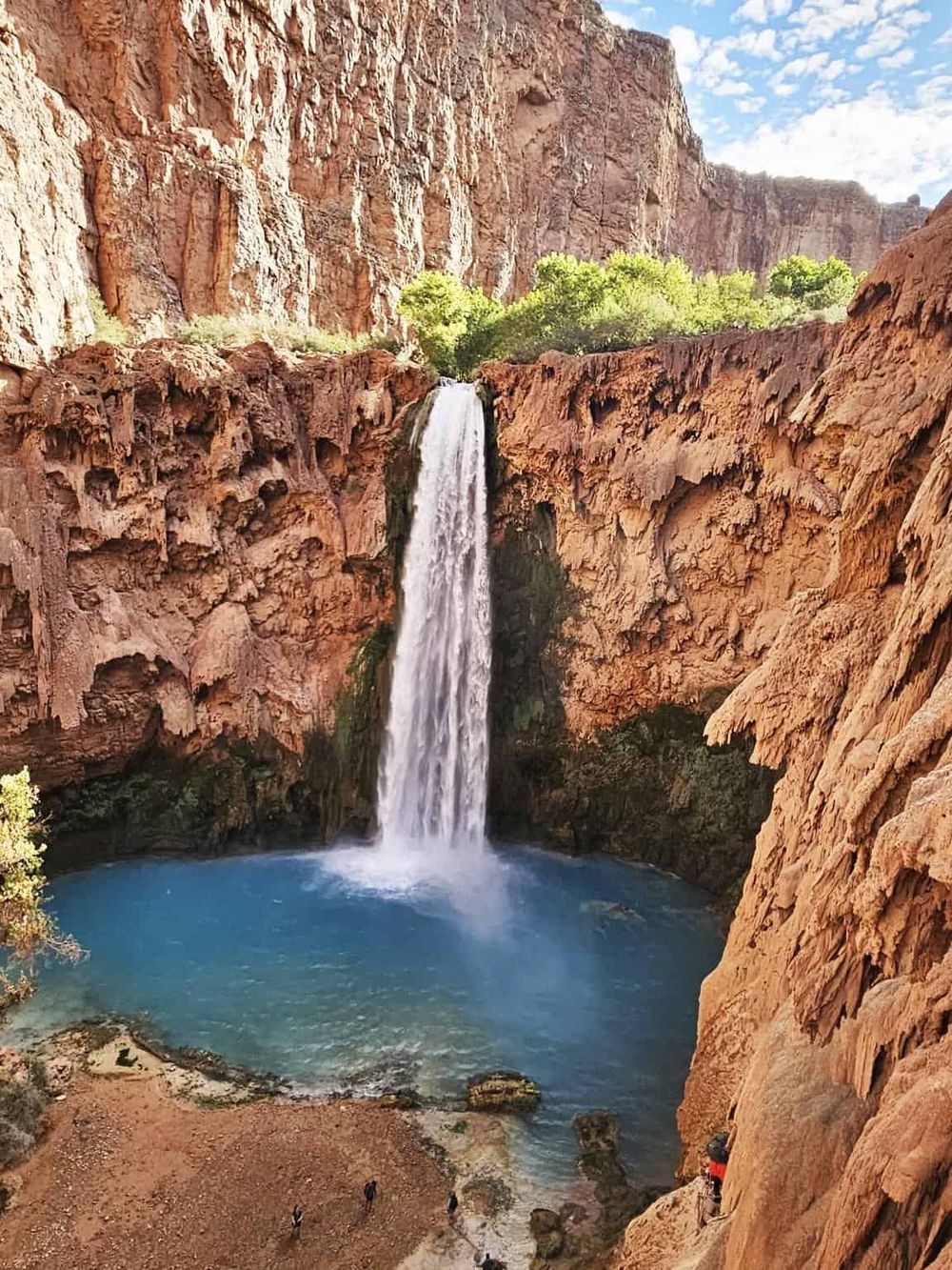 Majestic waterfall cascading into a blue pool amidst red rock cliffs at a canyon.