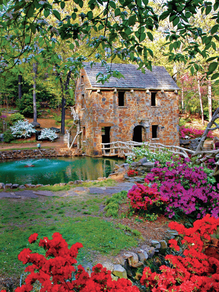 Charming stone millhouse surrounded by vibrant flowers and lush greenery in a serene garden setting.