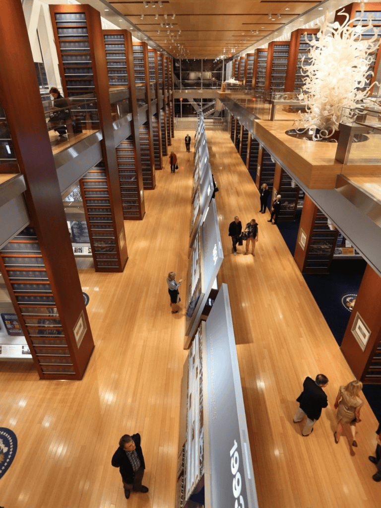 Aisle view inside Quest for Directions' expansive library with wood shelves and visitors exploring exhibits.