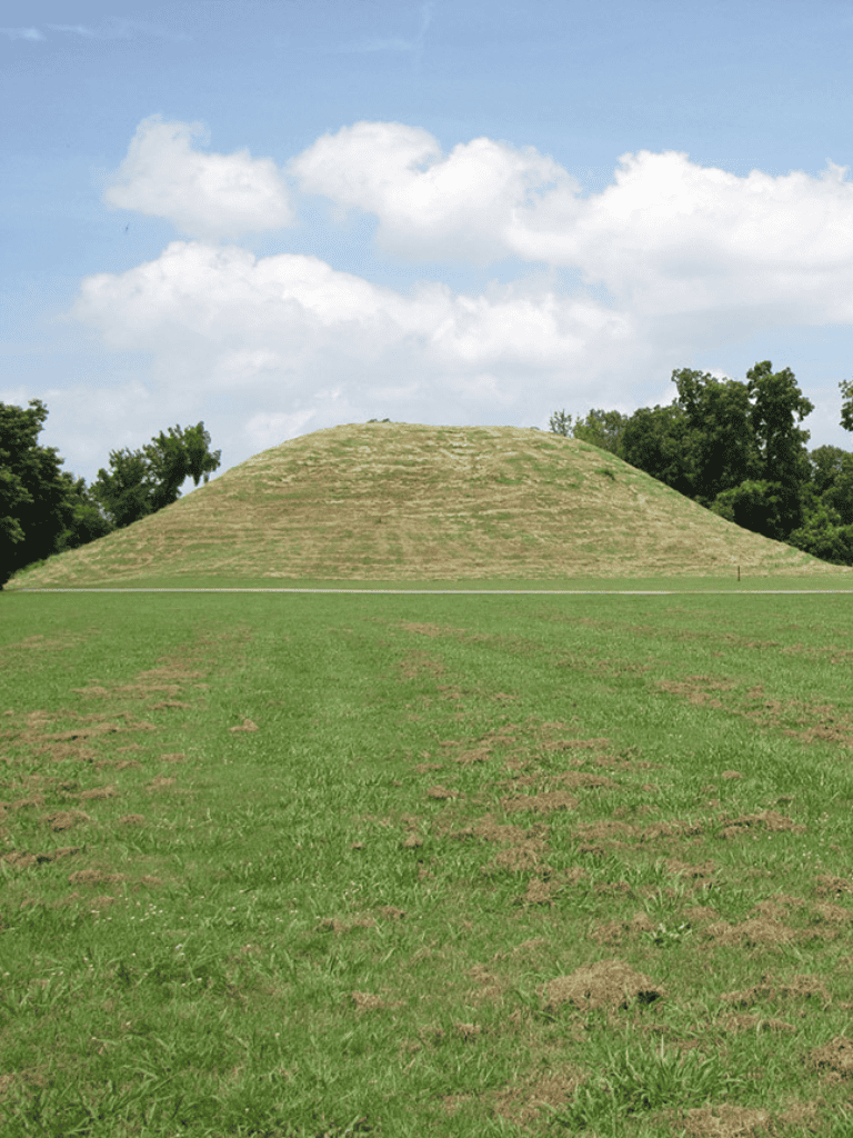 Ancient mound surrounded by green grass under partly cloudy sky, part of historic sites for exploration.