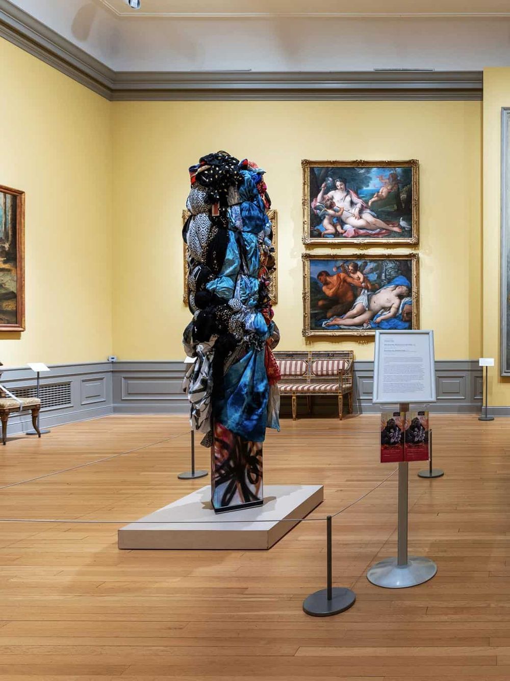 Colorful fabric sculpture in art museum with classical paintings in the background.