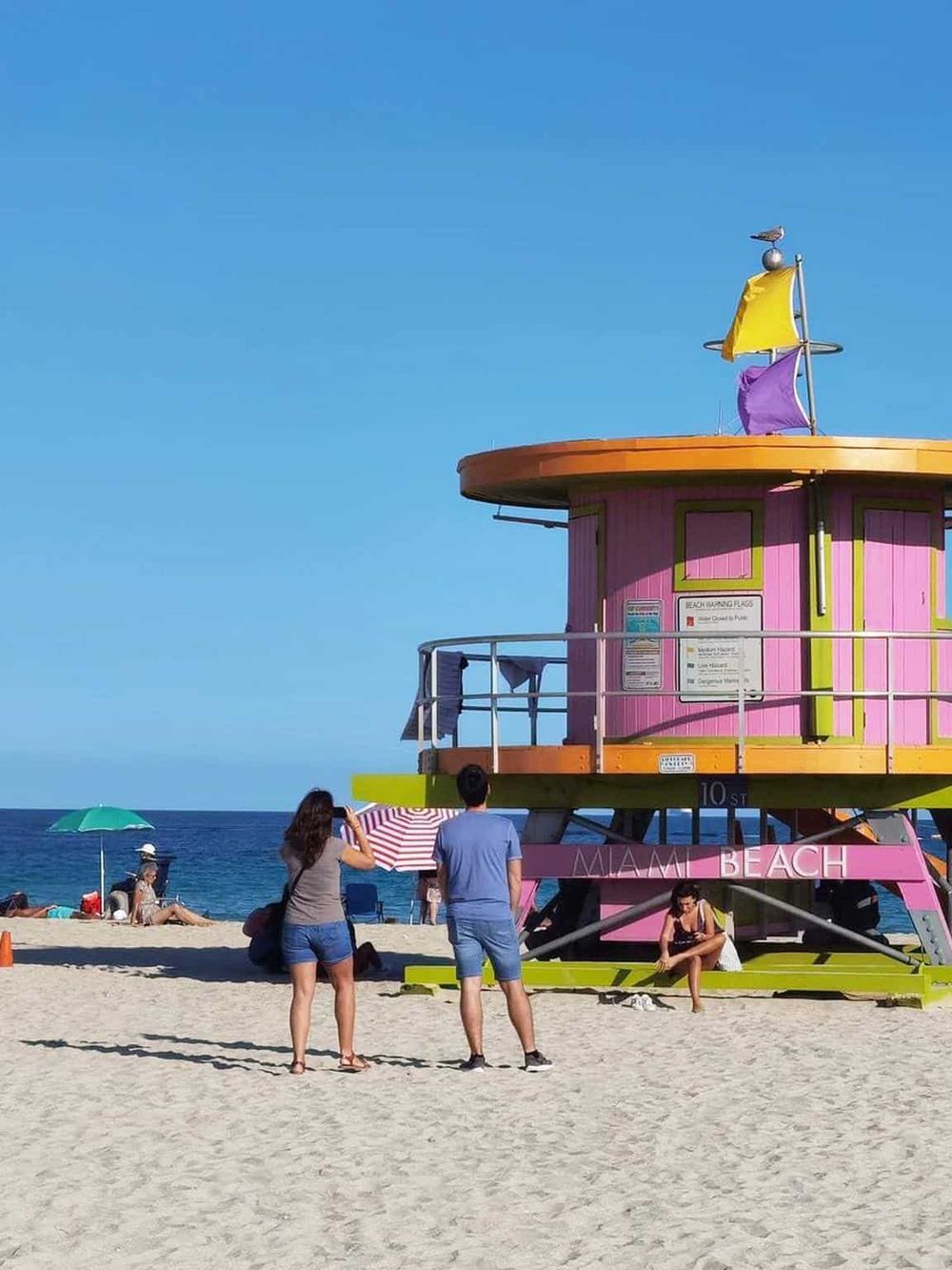 Colorful Miami Beach lifeguard tower on the sandy shore with people enjoying the sunny day.