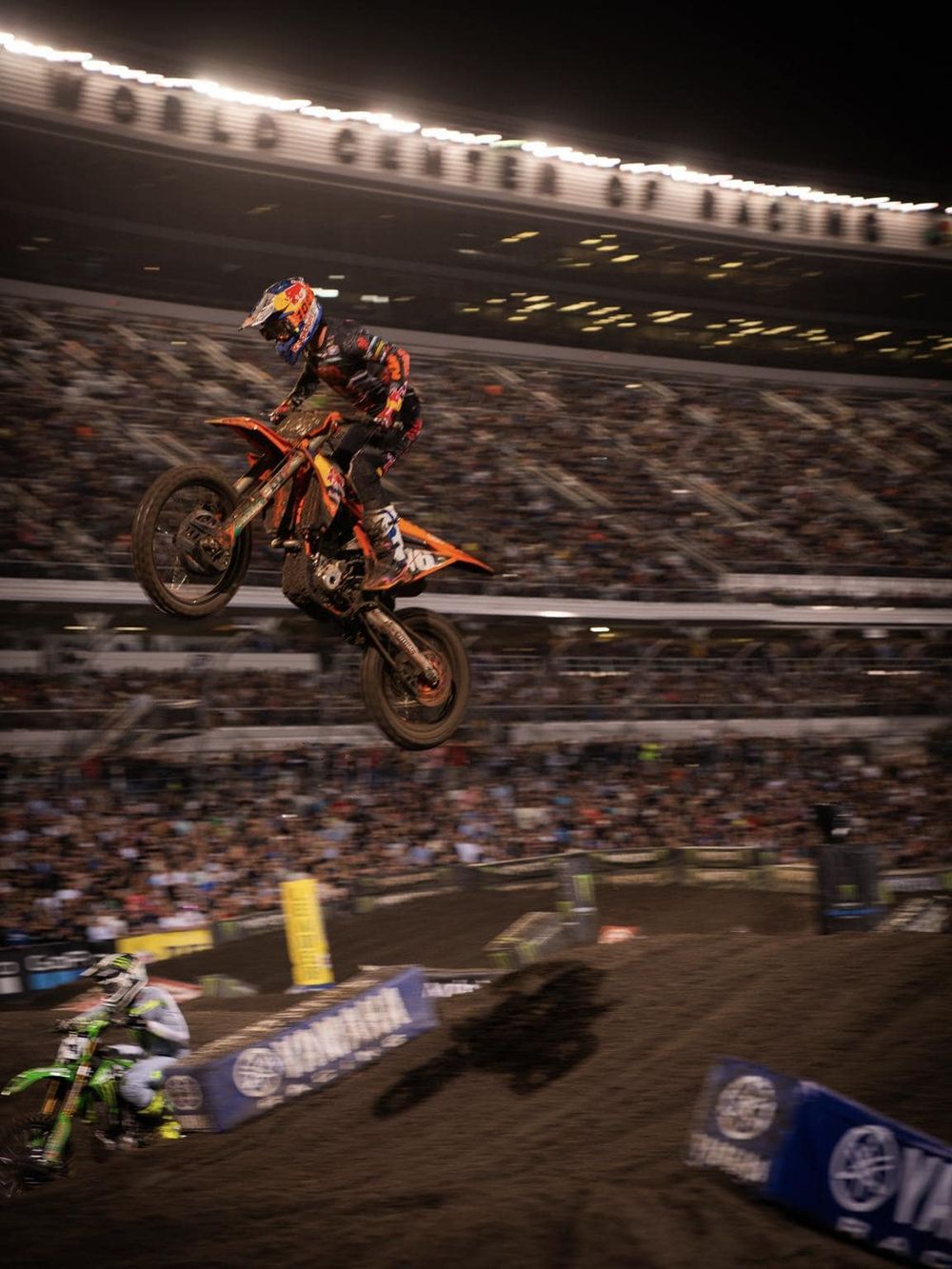 Motocross rider performing jump during night race at stadium, high-speed action.