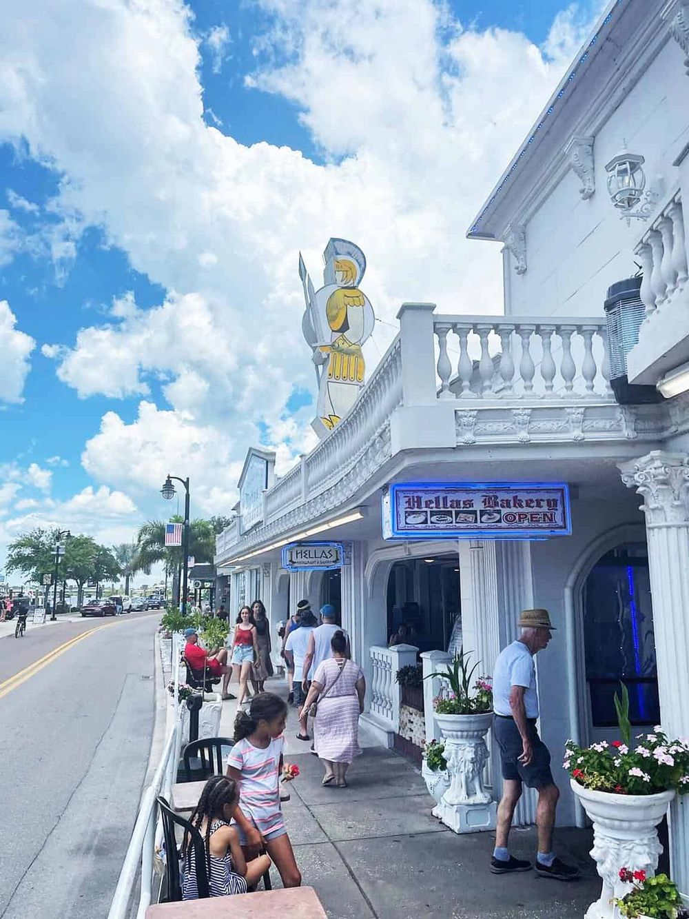 Colorful storefront on a sunny day with people dining and walking outside, showcasing a charming shopping and dining experience.