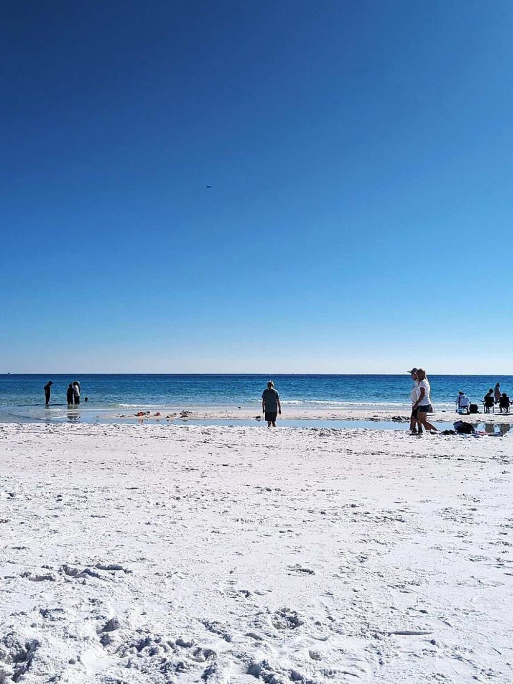 Sunny beach with white sand and blue ocean, people relaxing and enjoying the seaside.