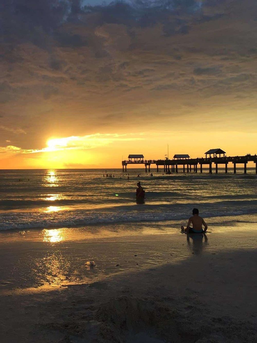 Relaxing beach sunset with pier, children playing in the water, and calming ocean views.