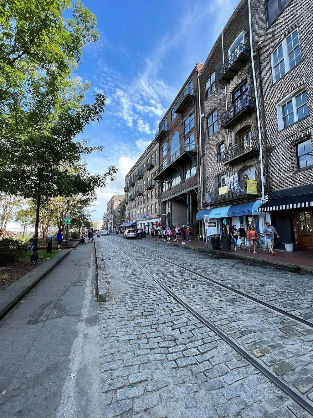 Charming city street with cobblestone tracks, historic buildings, and pedestrians enjoying a sunny day.