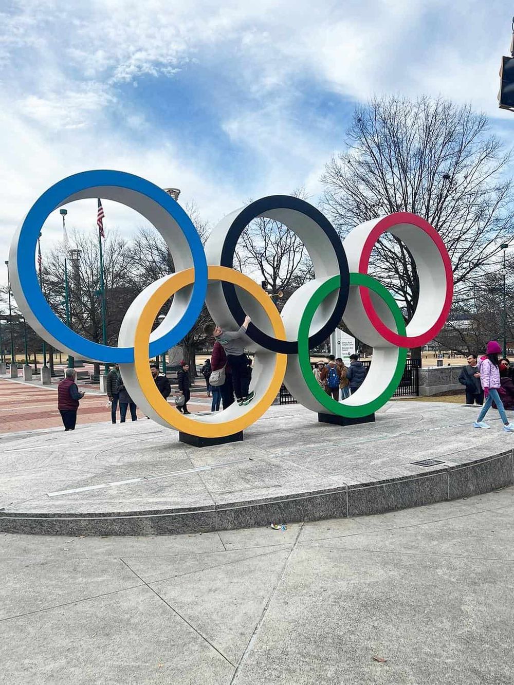 Colorful Olympic rings sculpture at a park with people, symbolizing sports and international unity.