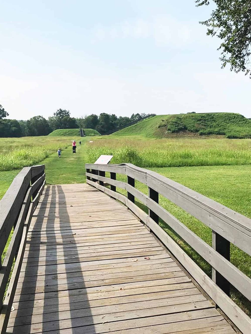 Scenic park with wooden bridge, green fields, and historical mounds, ideal for outdoor exploration and family activities.