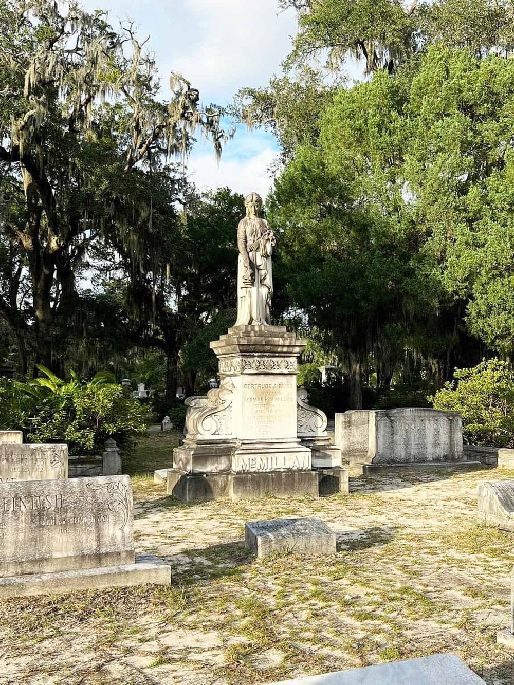 Historic cemetery with a prominent statue of a religious figure among lush trees and weathered tombstones.