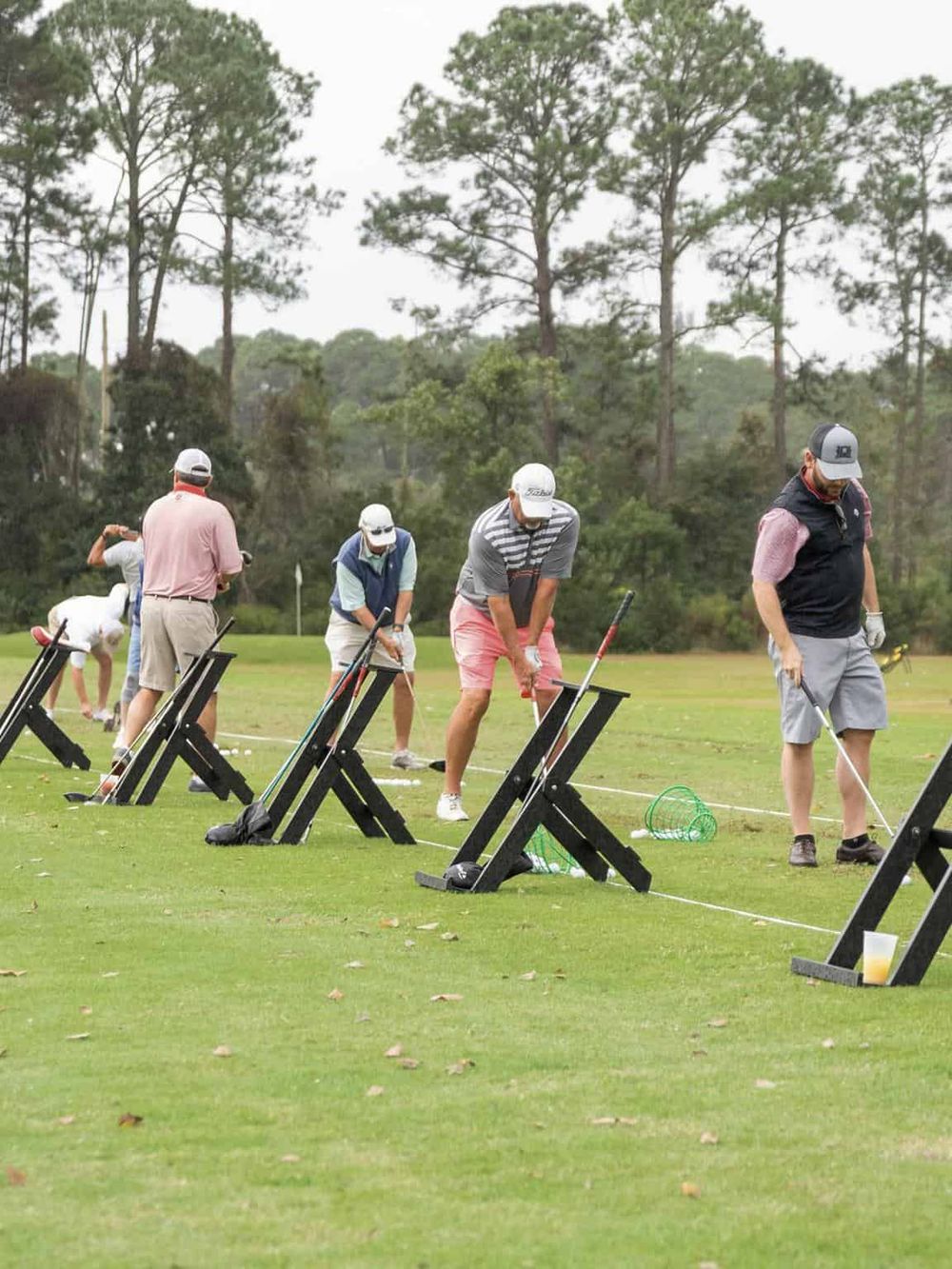 Golf training session on a lush green course, players practicing putting with alignment aids, surrounded by tall trees.