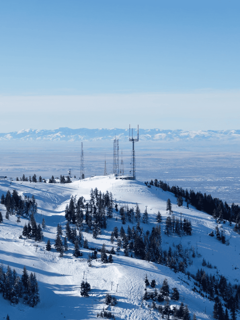 Snow-covered mountain landscape with communication towers and pine trees in winter.
