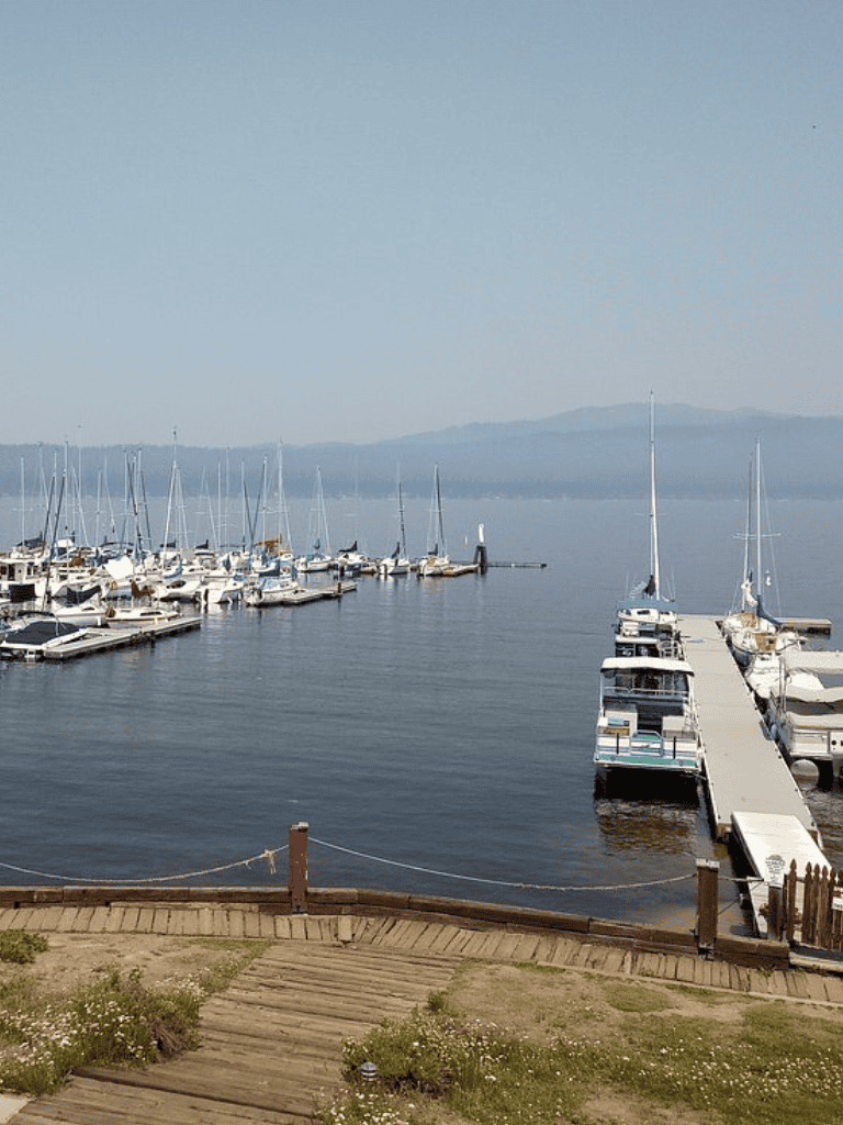 Boats docked at marina on calm water with mountains in background.