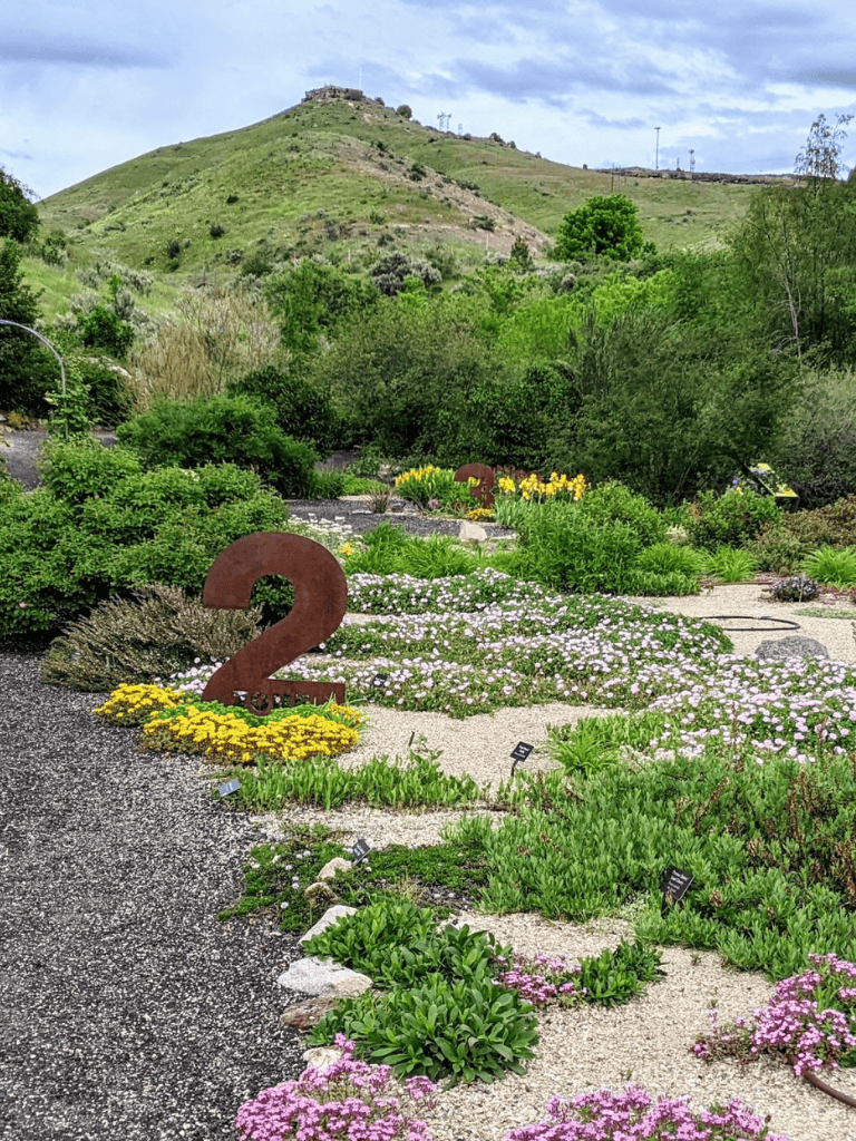 Colorful garden with "2" sculpture, lush greenery, and mountain backdrop at QuestForDirections.