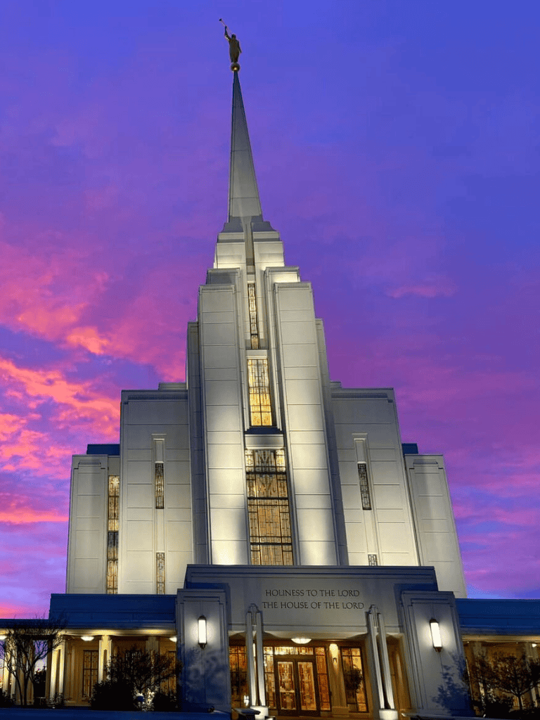 Brightens LDS Temple at sunset with illuminated angel Moroni statue at the top.