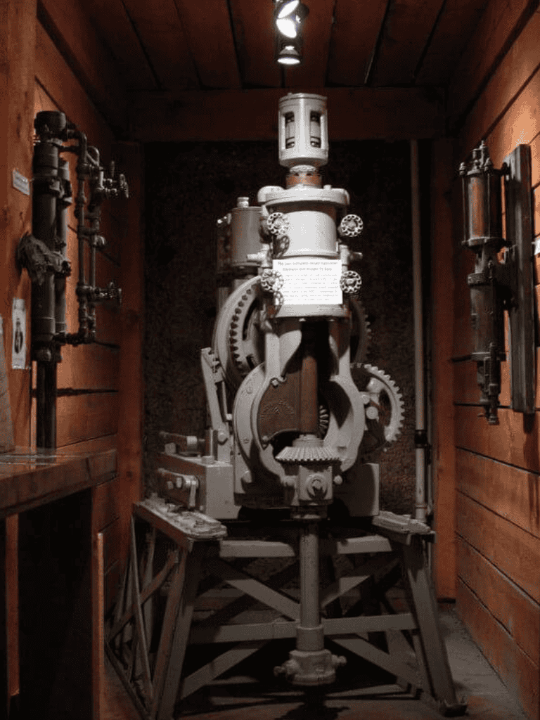Industrial gear mechanism display in a wooden-walled museum setting.