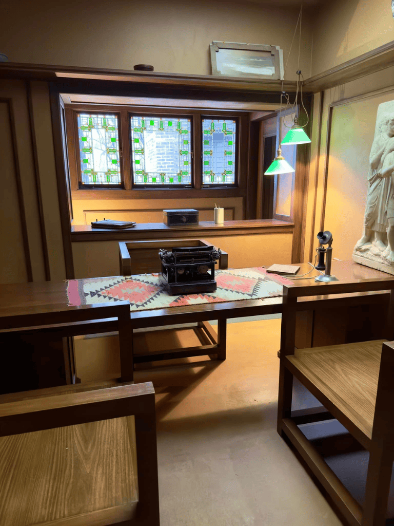 Antique typewriter on colorful table runner in cozy room with stained glass window and sculpture.