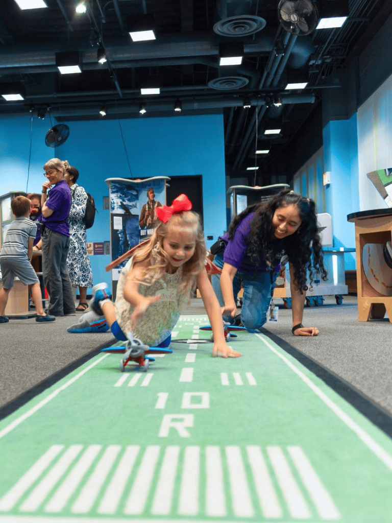 Colorful indoor kids' science and discovery play area with children engaging in hands-on activities.