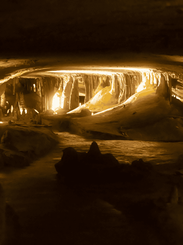 Mysterious underground cave with stalactites and stalagmites illuminated by soft lighting.