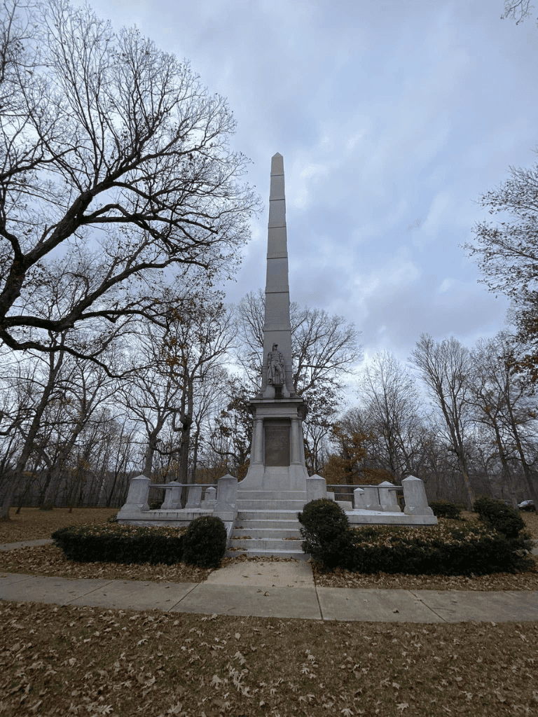 Eternal Flame Veterans Memorial obelisk in a park with trees and fall foliage.