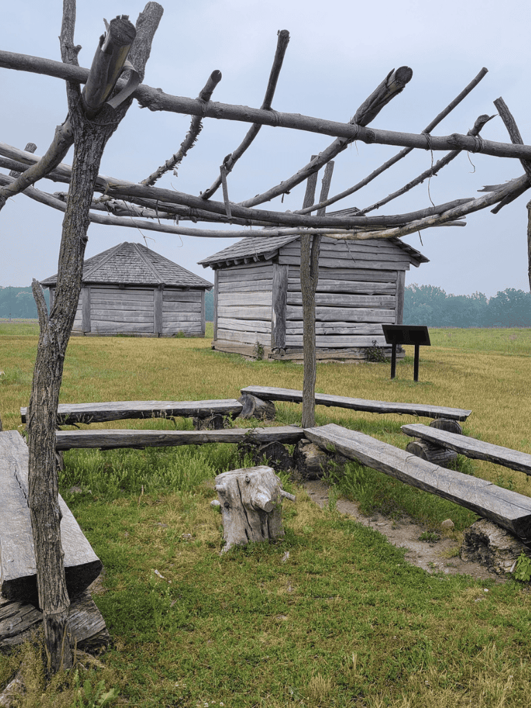 Rustic outdoor wooden shelter with benches and a historic village setting for educational tours.